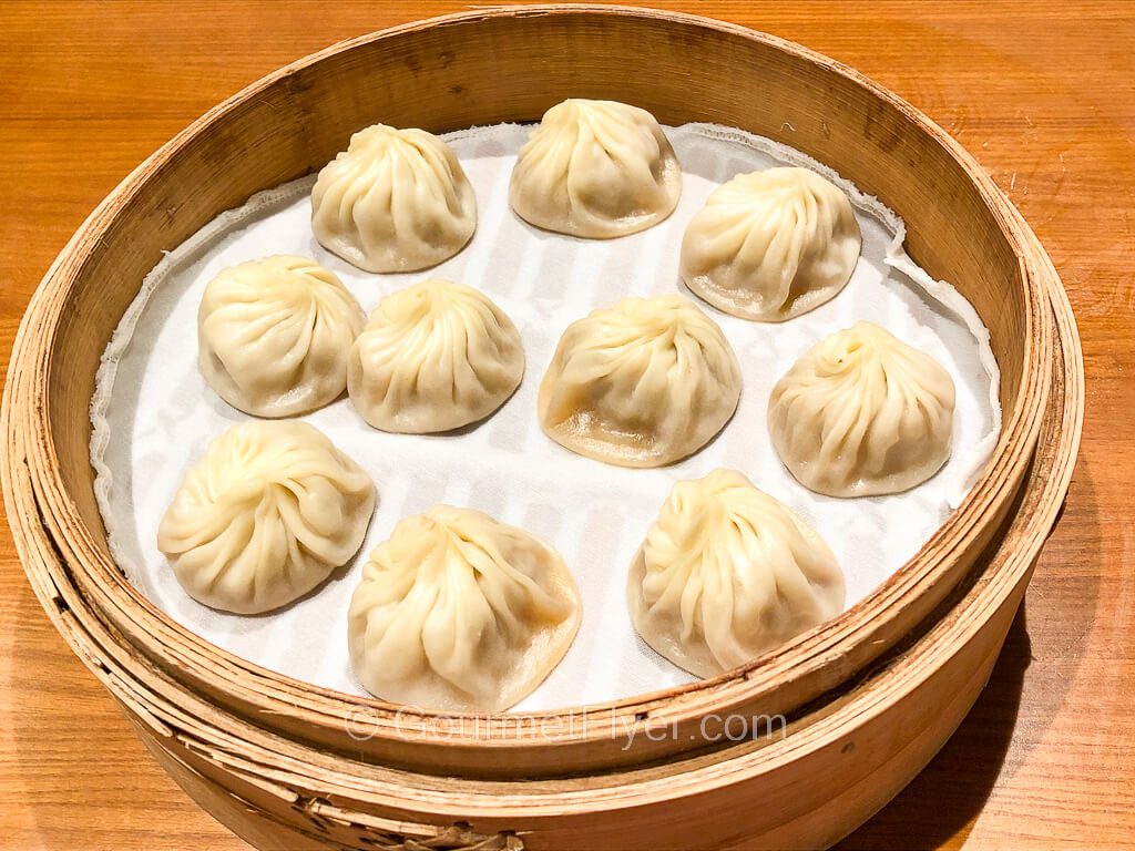 A bamboo steamer basket contains 10 cooked dumplings.