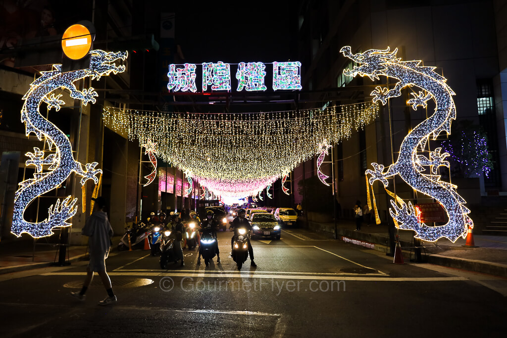 Two brightly lit dragons line each side of a street in an intersection, accompanied by numerous lights hung across the street.