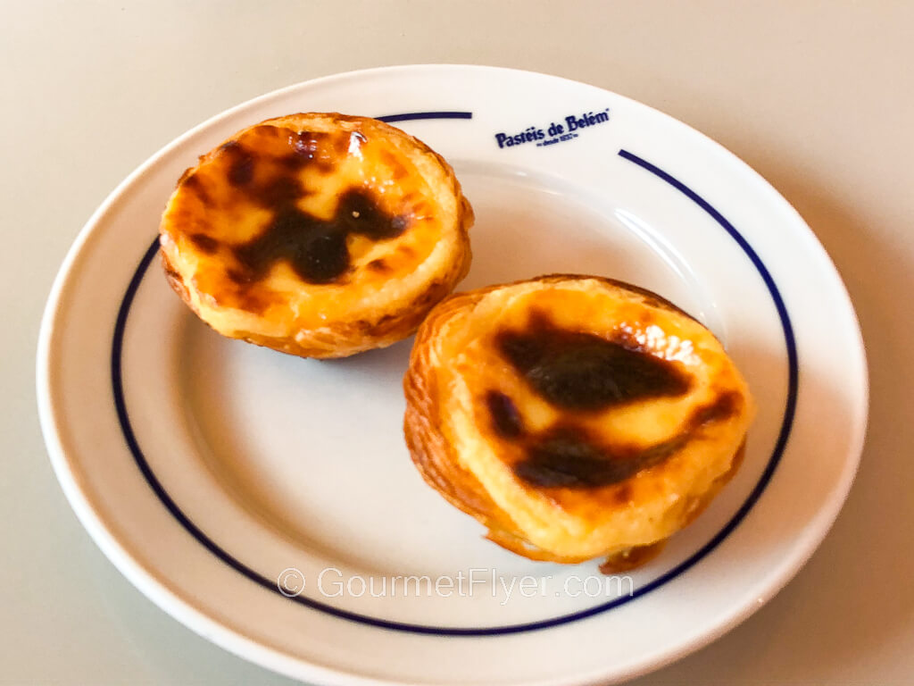 Two egg tarts with a charred top are served on a small white plate.