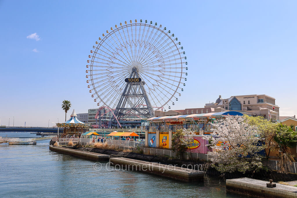 A giant Ferris wheel displaying the current time is seen in the background of the harbor.