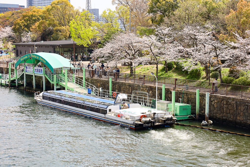 A tourist boat is parked at a dock on a river lined with plenty of colorful trees.