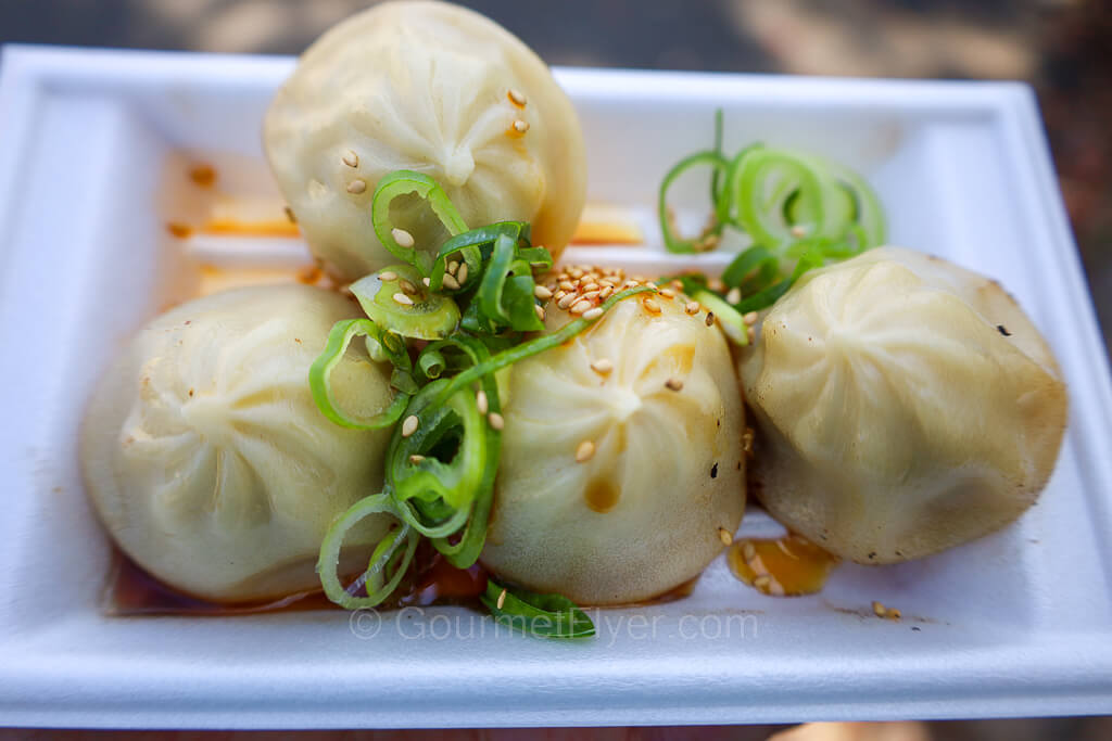 Four dumplings on a plate is garnished with green onions and sesame.