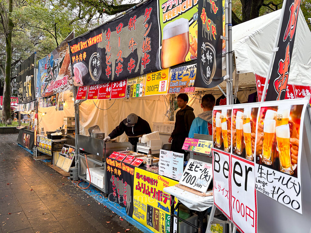 A food booth displays a large sign advertising beers at 700 yen and other foods on the menu.