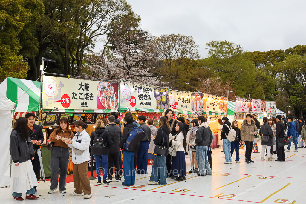 Customers are visiting a row of food booths with colorful tents and signs.