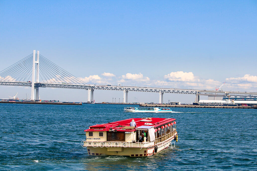 A boat sails toward a bridge in the harbor of a city.