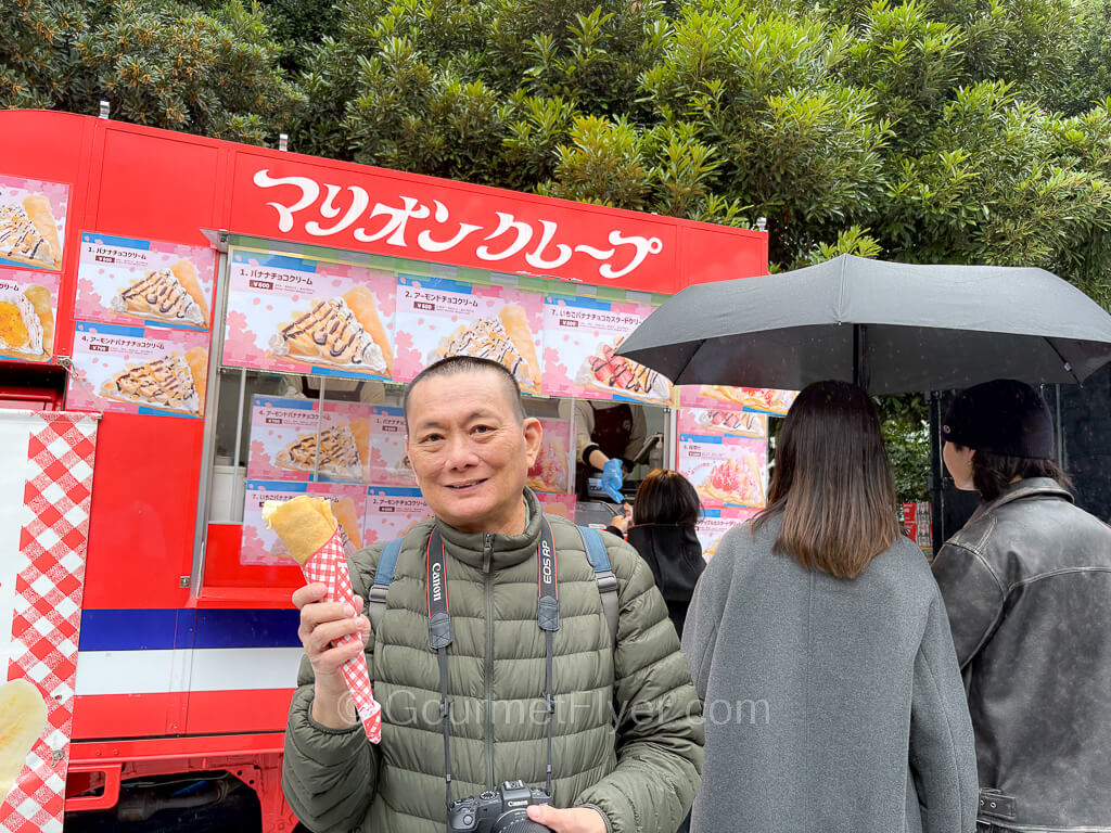 The blogger Gourmet Flyer poses with a crepe in his hand, with a food truck in the background.