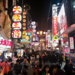Moderately priced iconic cultural places to eat in Osaka is shown in the heart of Dotonbori where huge crowds roam the streets under bright neon signs.