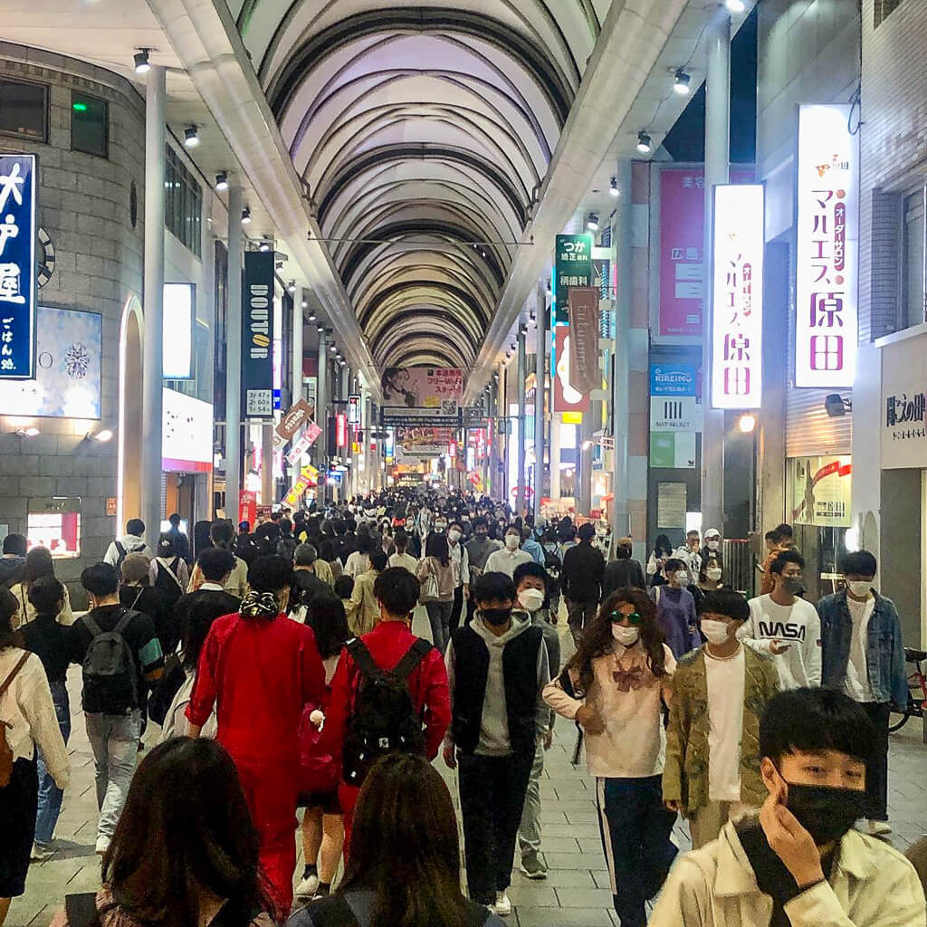 A long shopping street with stores on both sides is packed with people.