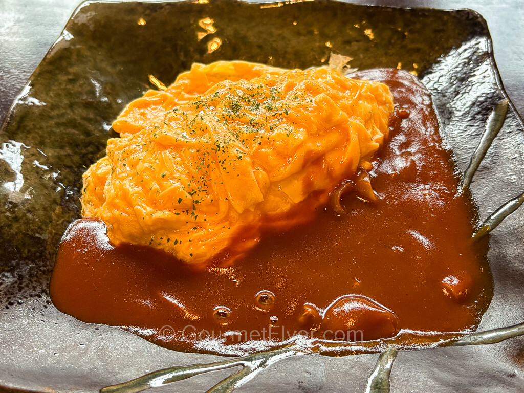An entree covered with moist scrambled eggs is served with a brown gravy on the side.