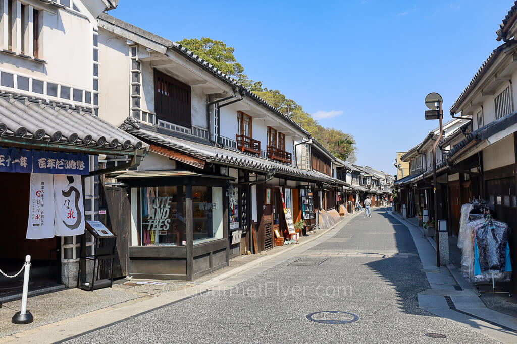 Two rows of historical two-story buildings line an empty street under a blue sky.
