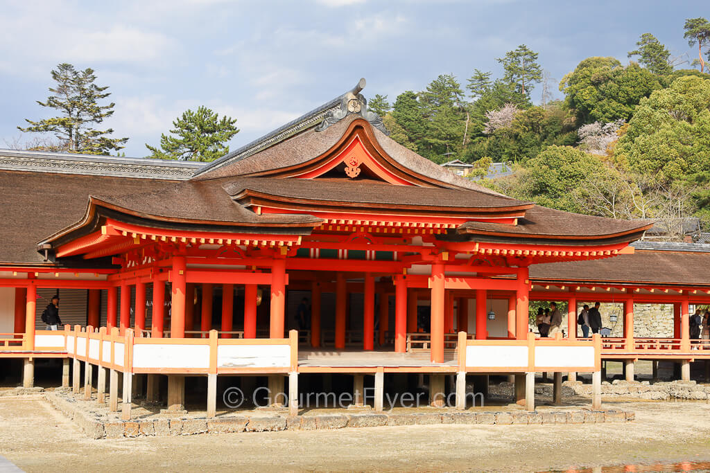 A shrine built with tall red cylindrical pillars has an elevated walkway above the sand.