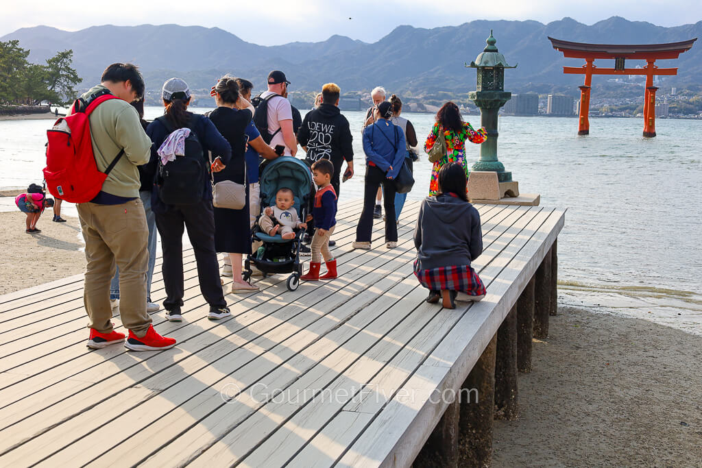 Tourists queue up to take photos at the end of a boardwalk with a clear centered view of the torii gate.