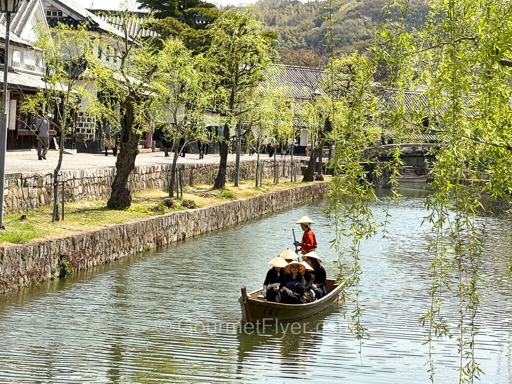 A boat carrying passengers sails on a waterway with green willow branches hanging from above.