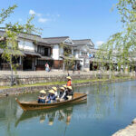 Day trip to Kurashiki features a boat sailing on a river with scenic traditional buildings in the background.