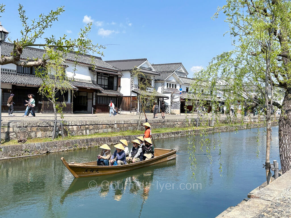 Day trip to Kurashiki features a boat sailing on a river with scenic traditional buildings in the background.