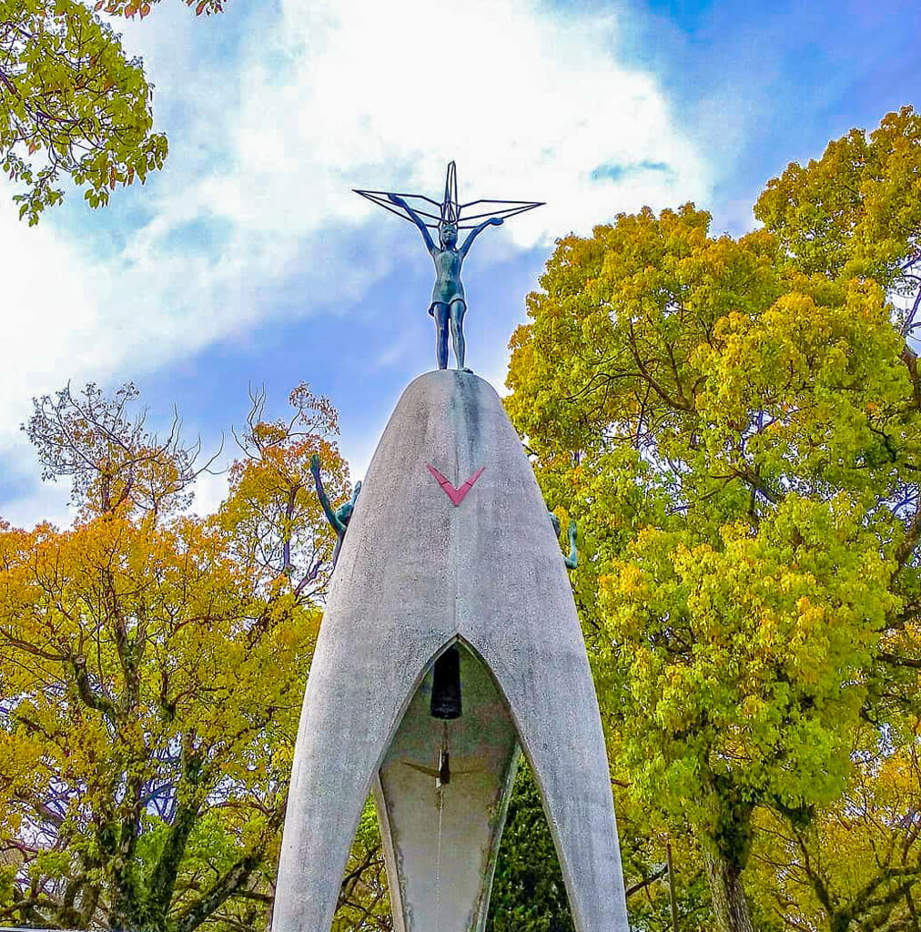 A monument has a child on top with her arms raised up high supporting what appears to be an origami crane.