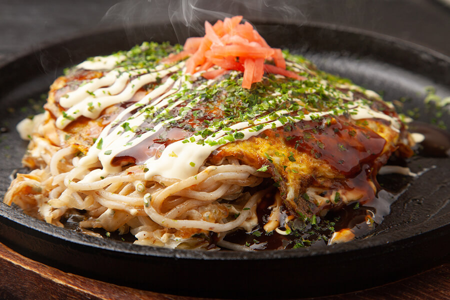 A cast iron hot plate contains a thick slab of food topped with mayonnaise and parsley.