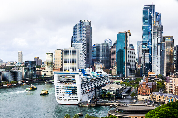A cruise ship is docked in the harbor of Sydney against a backdrop of the city's skyline.