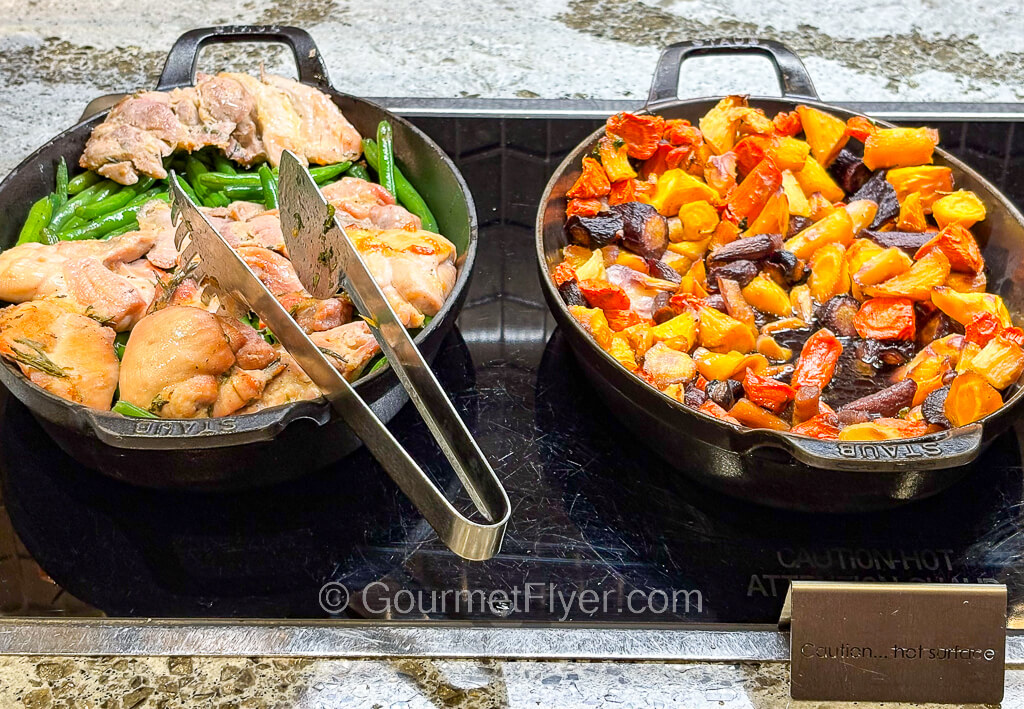 A pan of cutup chicken pieces on the left is accompanied by a pan of colorful vegetables on the right.
