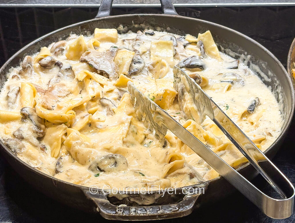 A large wok like serving bowl is filled with pasta in a creamy white sauce.