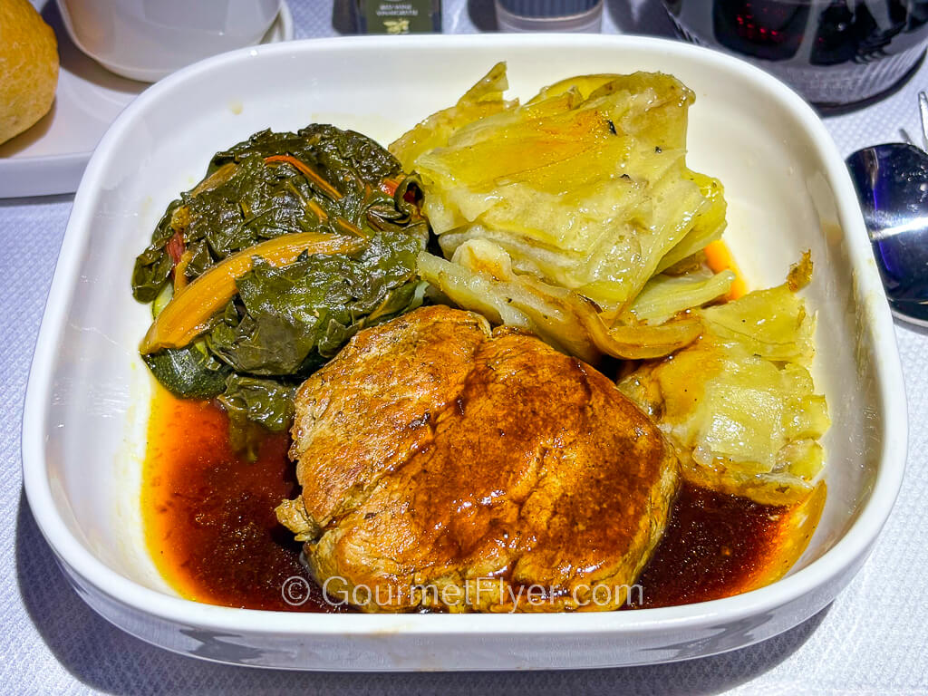 A steak is served with plenty of gravy and accompanied with vegetables.