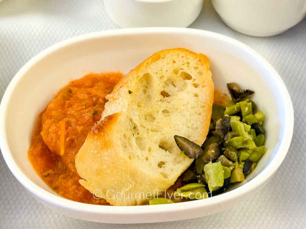 A dish of tomato puree is accompanied by a slice of toasted baguette.