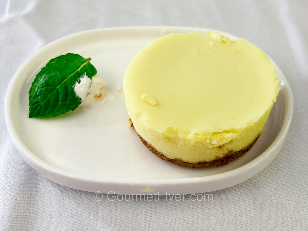 A greenish yellow round cake has a smooth top and a cookie crust bottom.