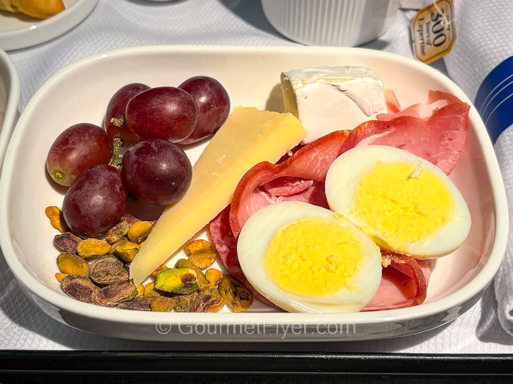 A pair of halved hard-boiled eggs is served on top of deli meat slices accompanied with grapes and garnished with nuts.