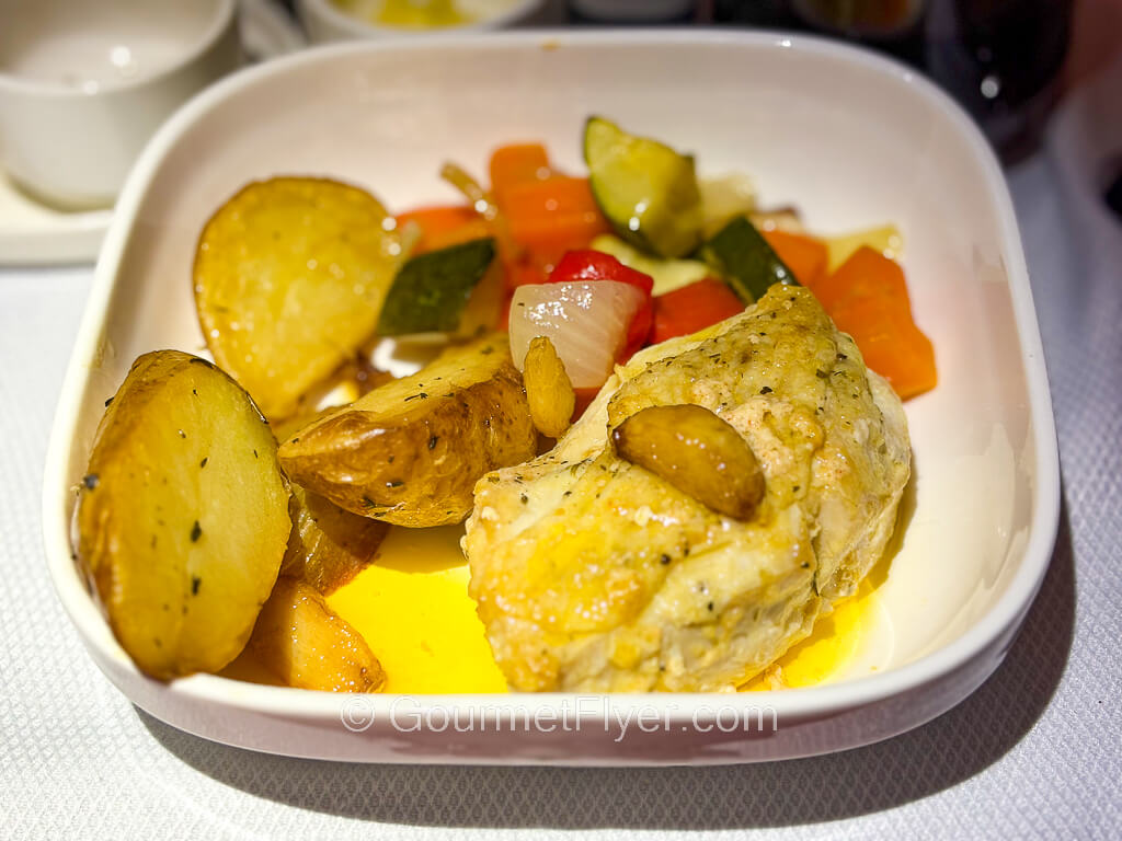A chicken breast on a plate is accompanied by potatoes and vegetables.