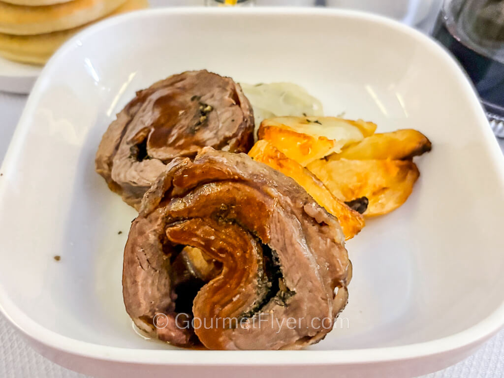 Two rolled-up pieces of meat are accompanied by potatoes wedges on a plate.