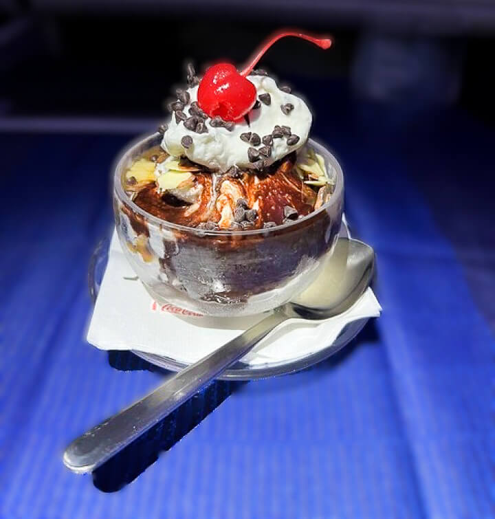 An ice cream sundae served in a glass container has many toppings, including whipped cream and a cherry on top.