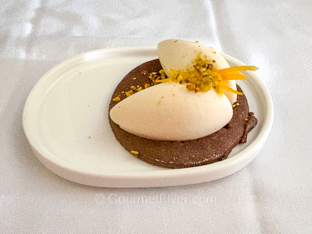 A cookie like cake is garnished with two lumps of creamy toppings.