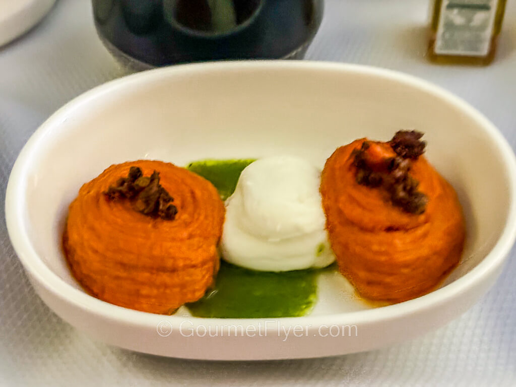 Two pieces of a reddish mousse is served on a plate with fresh cheese.