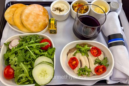 A review of the food served on United Polaris International Business Class features an appetizer tray with meat topped with cream sauce, a green salad, bread, butter, and a glass of red wine.