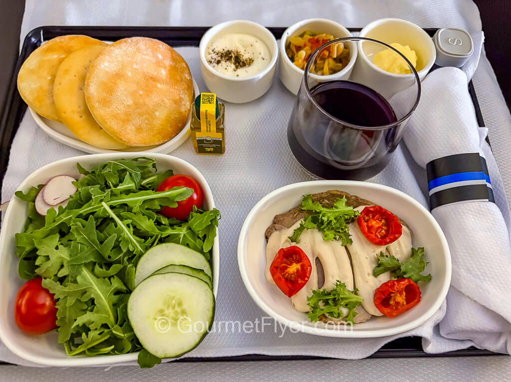 A review of the food served on United Polaris International Business Class features an appetizer tray with meat topped with cream sauce, a green salad, bread, butter, and a glass of red wine.