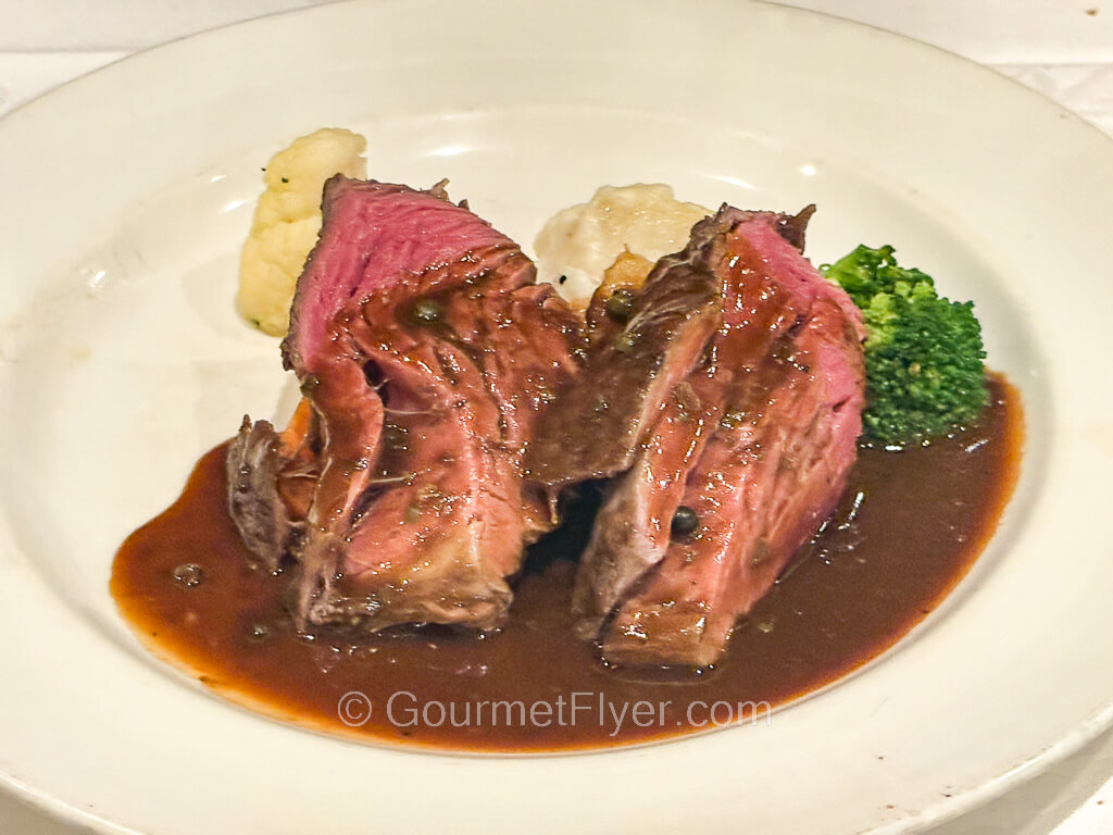 Two slices of medium rare steaks are served with brown gravy and vegetable sides.