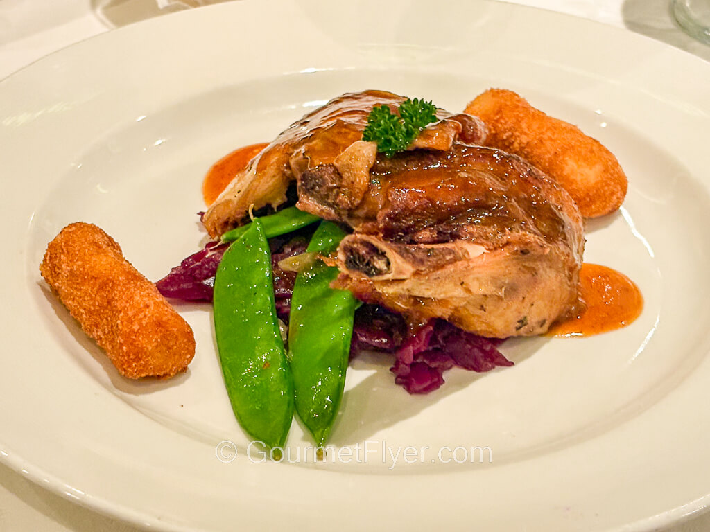 A roasted duck leg is served with gravy and garnished with colorful vegetables.