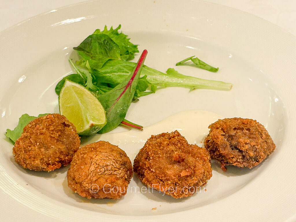 Four pieces of fried mushrooms are accompanied by a wedge of line and some green vegetables.