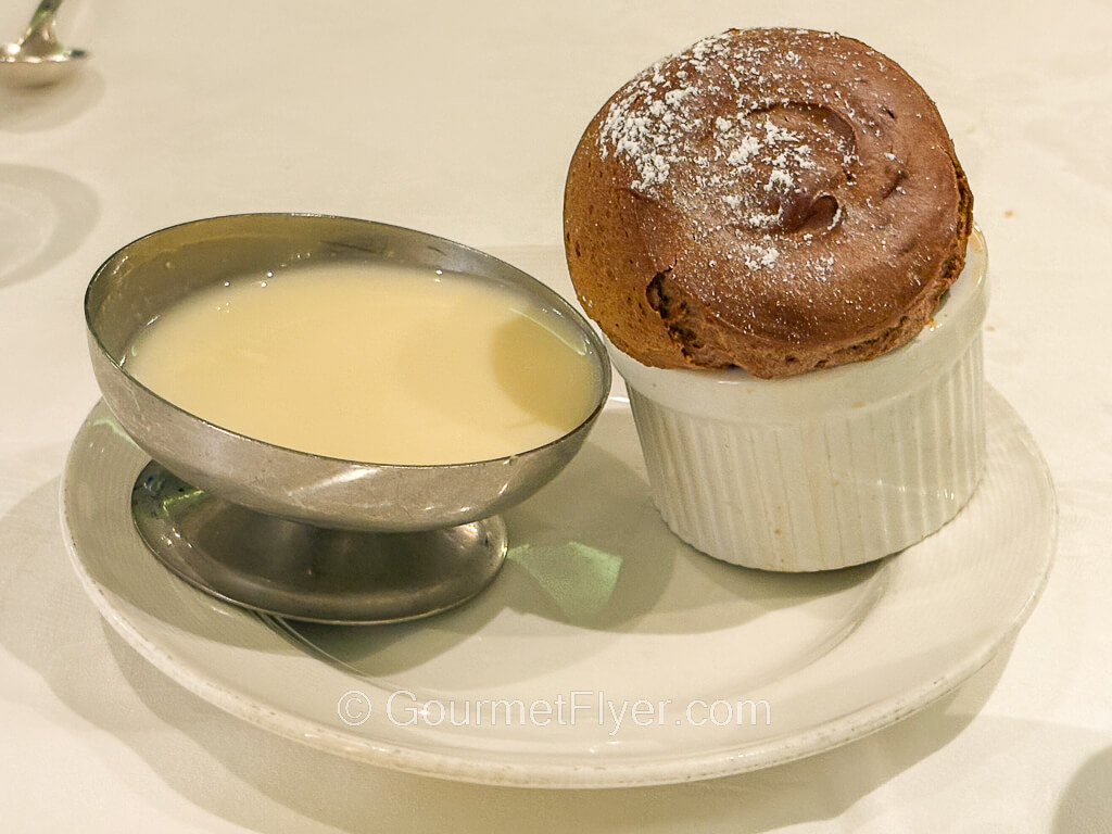 A souffle type of bakery in a white ceramic bowl is accompanied by a white creamy sauce.