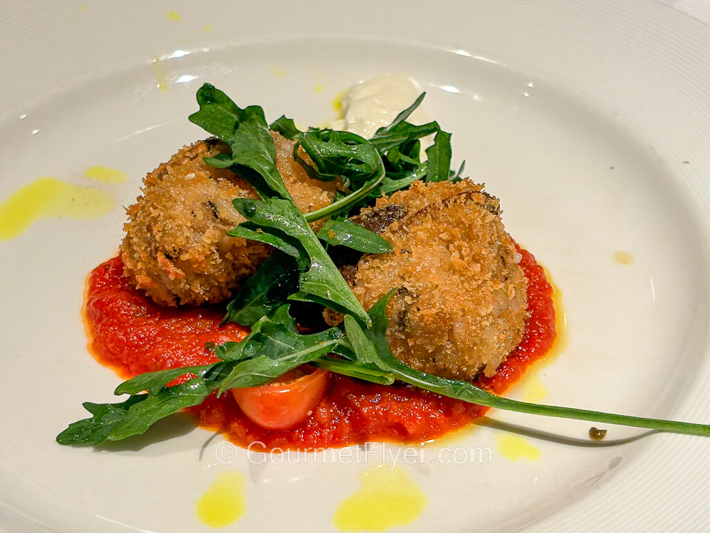 A pair of fried dumplings sit atop a pool of tomato sauce.