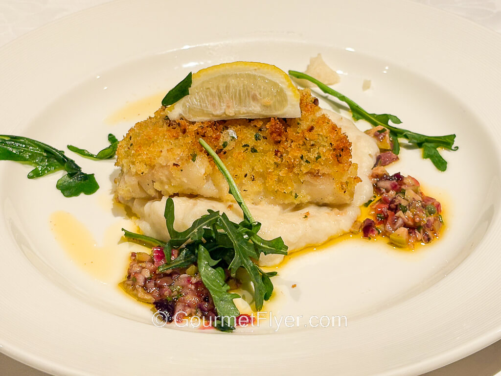 A piece of fried fish is served with mashed potatoes and a wedge  of lemon.