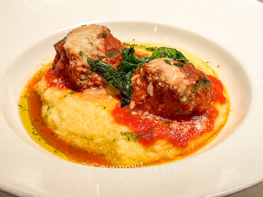 Two meatballs are served on a plate with tomato sauce, potatoes, and spinach.