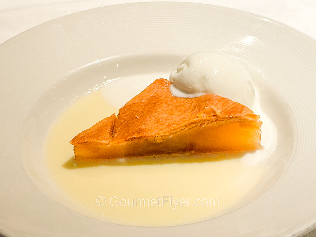 A slice of fruit pie is served with cream sauce and a scoop of vanilla ice cream.