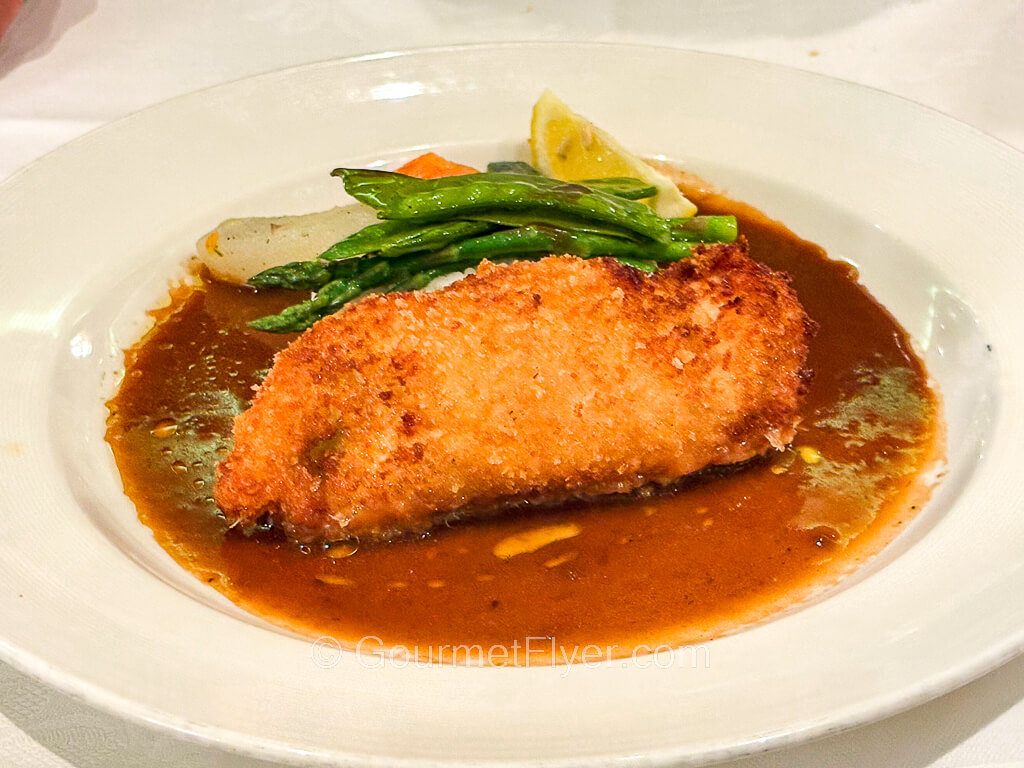 A piece of fried breaded meat is drenched in a pool of brown gravy and accompanied by asparagus.