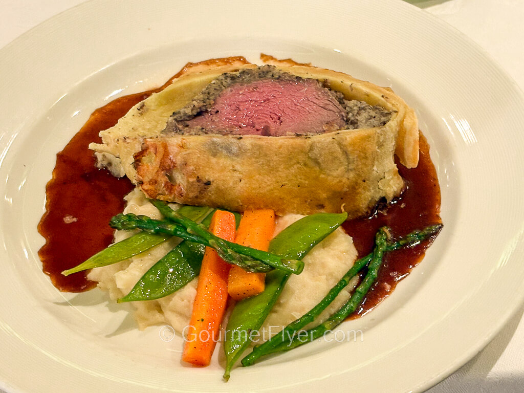 A pink slab of beef filet is wrapped in a breaded crust and served with a brown gravy.