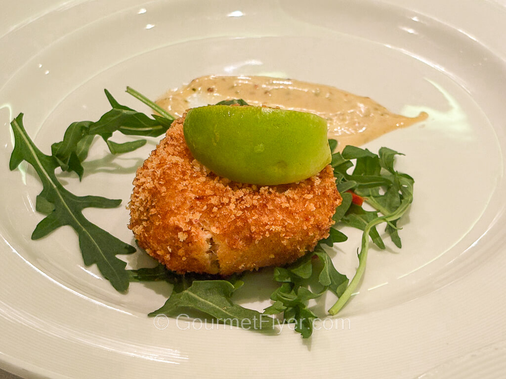 A fried seafood cake with golden brown bread crumb crust is topped with a wedge of lime.