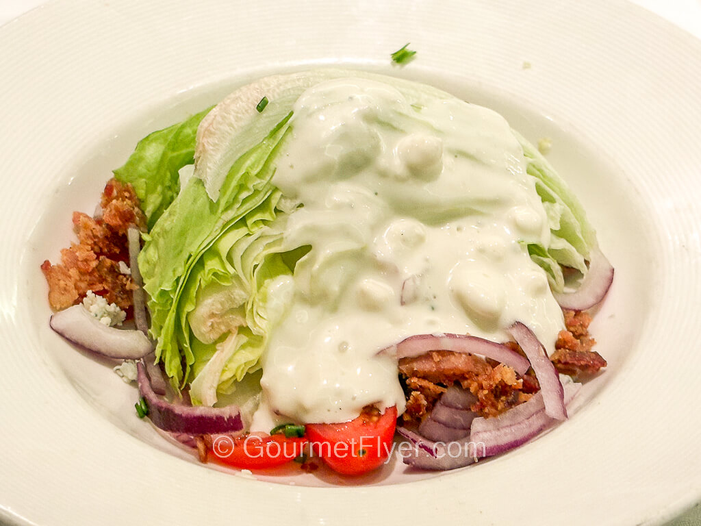 A wedge of iceberg lettuce is covered with a creamy dressing and accompanied by stripes of red onion.