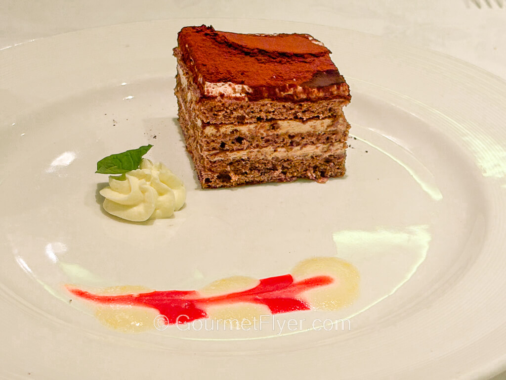A square piece of chocolate cake is garnished with colorful creams on a plate.