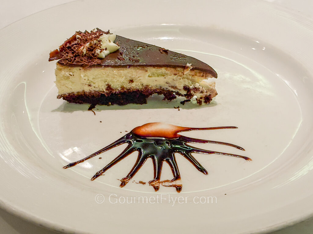 A slice of cheesecake is beautifully decorated with chocolate syrups on a plate.