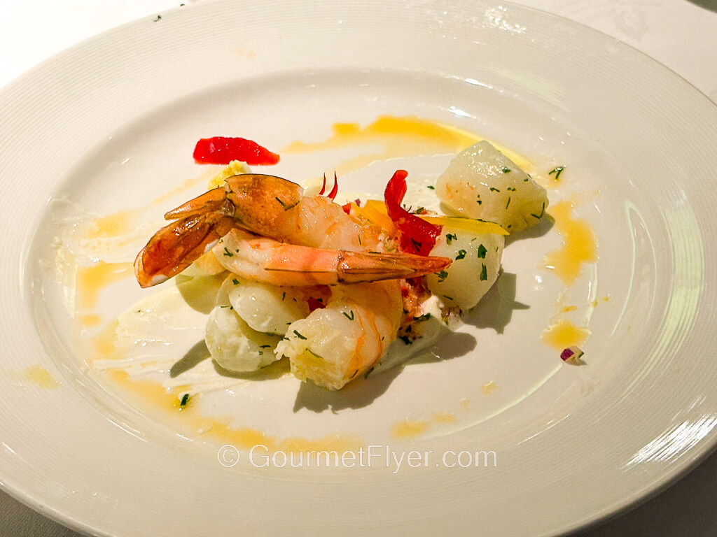 Two deshelled shrimps are accompanied by a about a half dozen of tiny scallops.